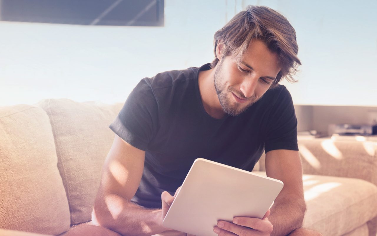 Arvato Systems_Commerce_Man on couch looking on tablet smiling Arvato Systems_Commerce_Man on couch looking on tablet smiling